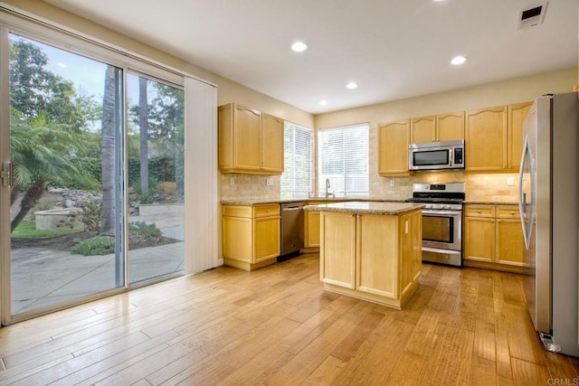 kitchen with stainless steel appliances, tasteful backsplash, light wood finished floors, and light brown cabinets