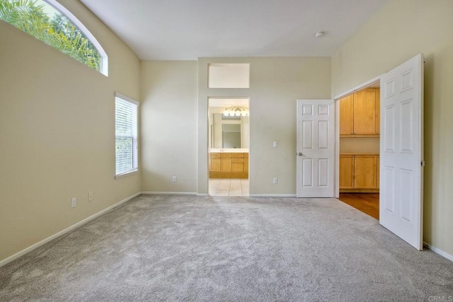 unfurnished bedroom with baseboards, carpet flooring, ensuite bath, and a walk in closet