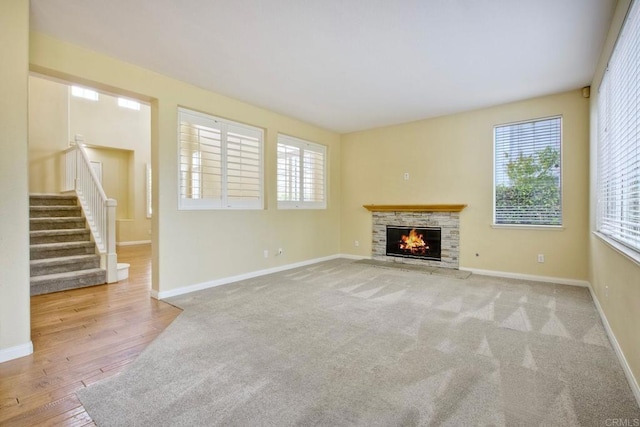unfurnished living room featuring a stone fireplace, stairs, baseboards, and wood finished floors