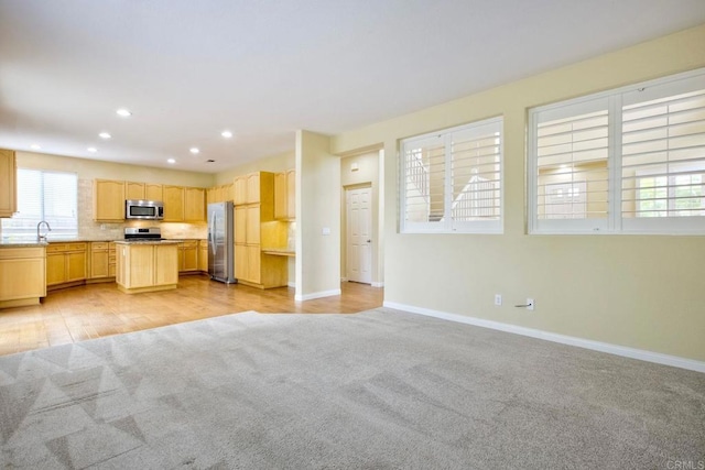 kitchen with light colored carpet, appliances with stainless steel finishes, light countertops, open floor plan, and light brown cabinets