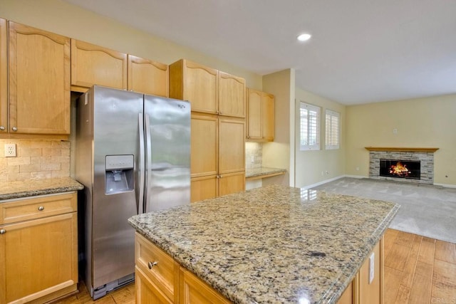kitchen with stainless steel fridge with ice dispenser, tasteful backsplash, light stone countertops, and a kitchen island