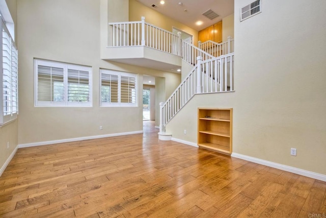unfurnished living room with stairs, visible vents, built in features, and hardwood / wood-style flooring