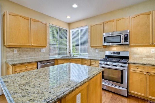 kitchen with a sink, light brown cabinets, stainless steel appliances, and light stone counters