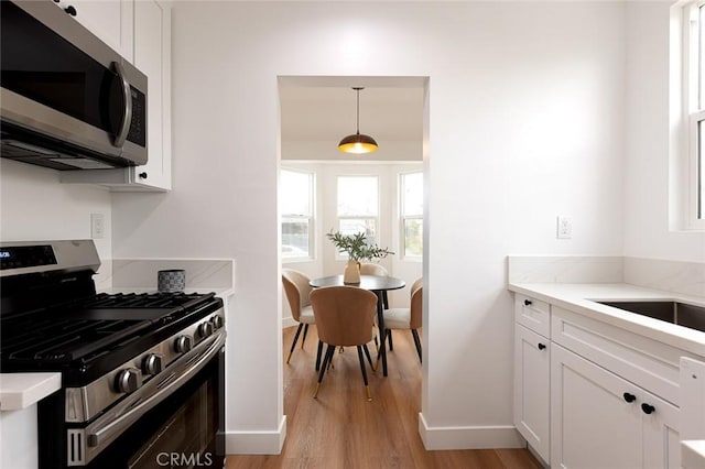 11714 S Spring St, Los Angeles, CA 90061 - kitchen with baseboards, light wood finished floors, appliances with stainless steel finishes, and white cabinets