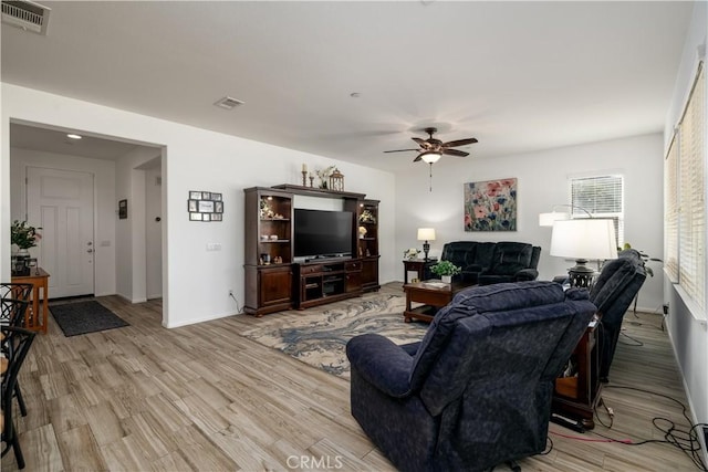 living room featuring ceiling fan, visible vents, baseboards, and light wood finished floors