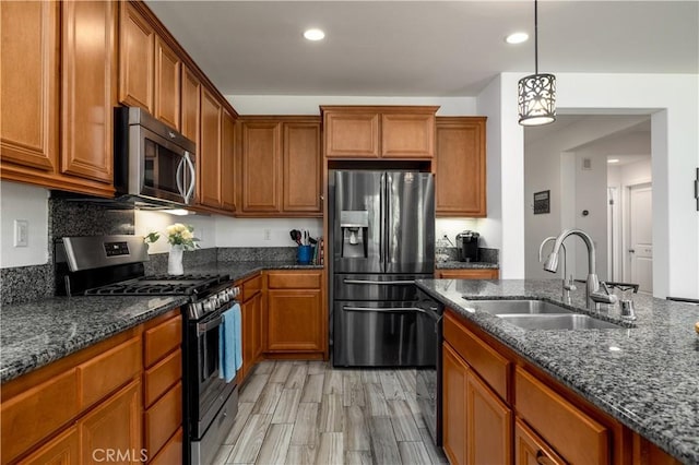 kitchen with recessed lighting, brown cabinets, a sink, dark stone countertops, and stainless steel appliances