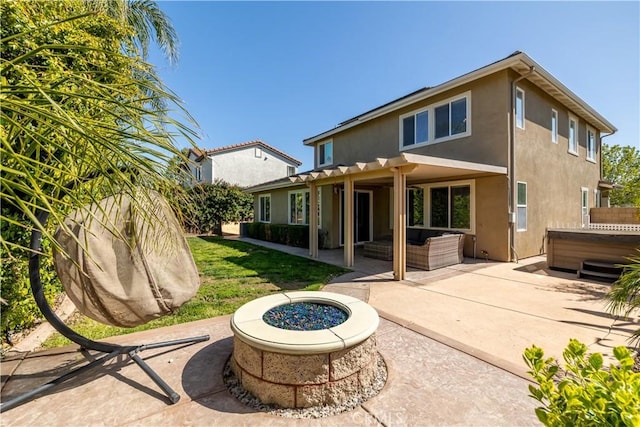 rear view of property featuring a hot tub, an outdoor fire pit, stucco siding, a patio, and a yard