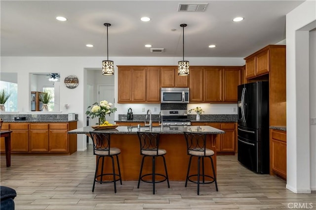 kitchen with appliances with stainless steel finishes, a kitchen breakfast bar, brown cabinetry, and visible vents