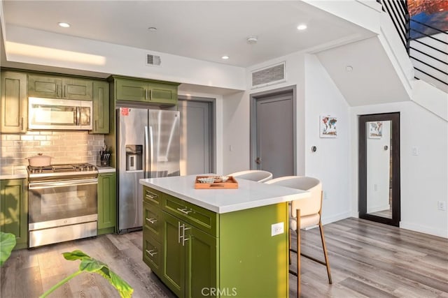 1055 S Serrano Ave Unit 502, Los Angeles, CA 90006 - kitchen with wood finished floors, a breakfast bar, green cabinetry, appliances with stainless steel finishes, and backsplash