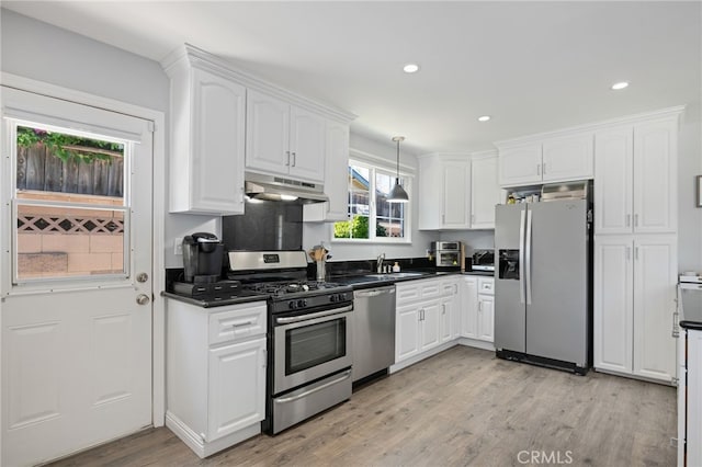 kitchen with dark countertops, a sink, white cabinets, under cabinet range hood, and stainless steel appliances