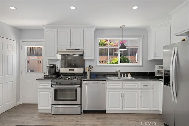kitchen featuring dark countertops, a sink, stainless steel appliances, white cabinetry, and under cabinet range hood