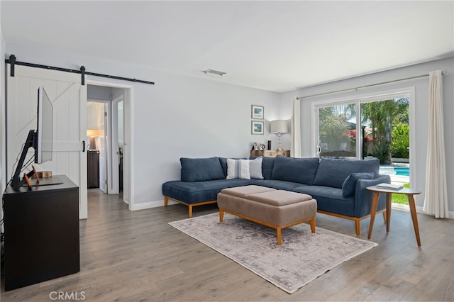 living area featuring baseboards, a barn door, wood finished floors, and visible vents