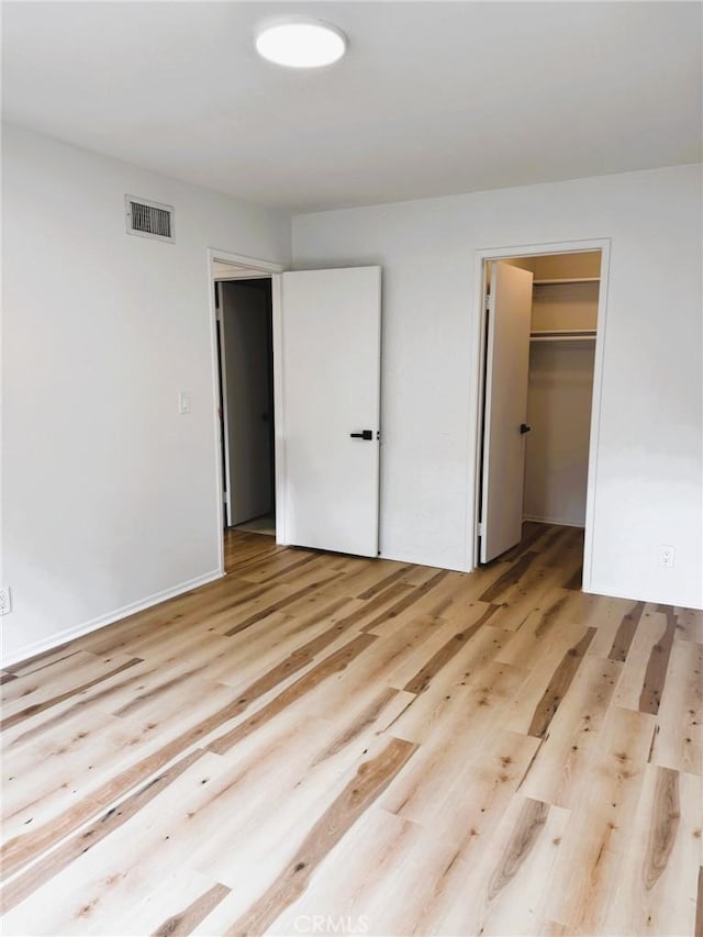 unfurnished bedroom featuring visible vents, a spacious closet, light wood finished floors, and a closet