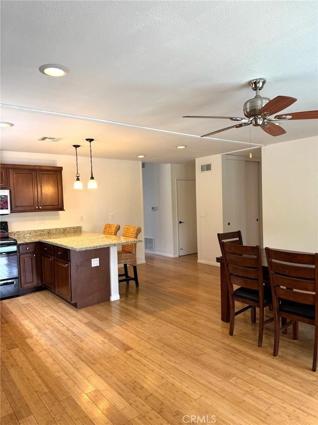 kitchen featuring ceiling fan, black electric range oven, white microwave, a peninsula, and a breakfast bar