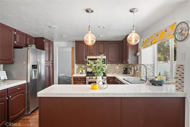 kitchen featuring appliances with stainless steel finishes, a sink, a peninsula, dark wood-type flooring, and backsplash