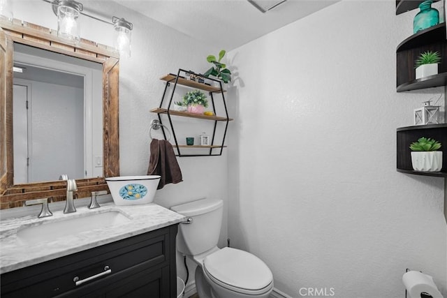 bathroom with baseboards, a textured wall, vanity, and toilet