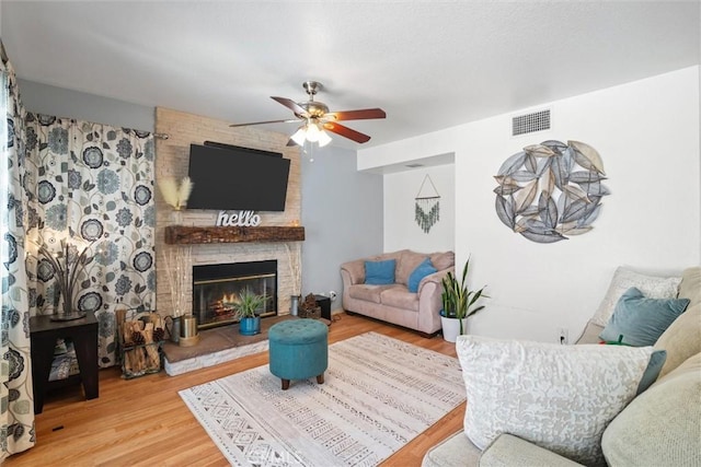 living area with a fireplace, a ceiling fan, wood finished floors, and visible vents