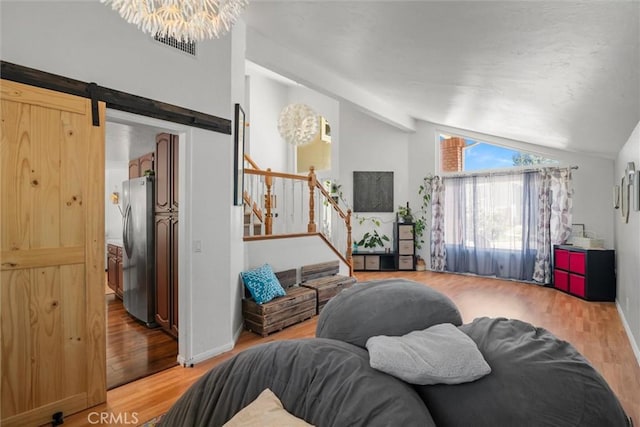 living area featuring a barn door, stairs, baseboards, lofted ceiling, and light wood-type flooring