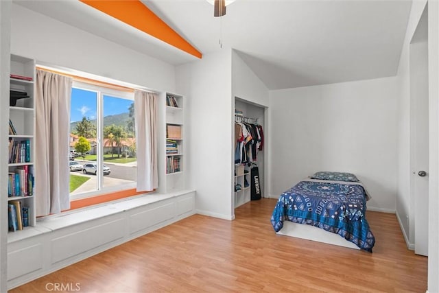 bedroom featuring ceiling fan, light wood-type flooring, baseboards, a closet, and lofted ceiling