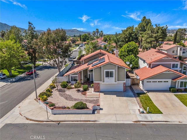 view of front of house featuring fence, a garage, roof mounted solar panels, a mountain view, and driveway