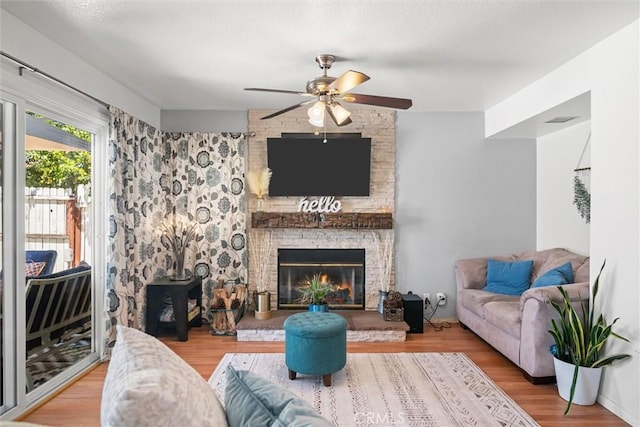 living area with visible vents, a wood stove, wood finished floors, a large fireplace, and a ceiling fan