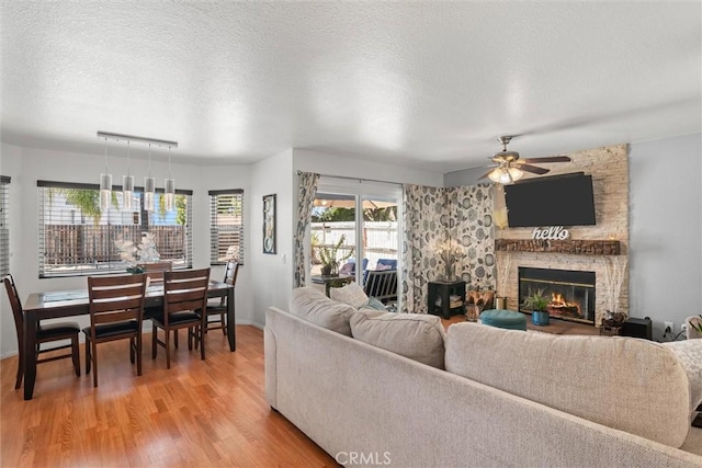 living area featuring ceiling fan, a textured ceiling, a fireplace, baseboards, and light wood-style flooring