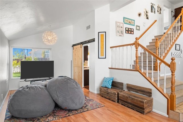 living area with a barn door, wood finished floors, lofted ceiling, visible vents, and stairway