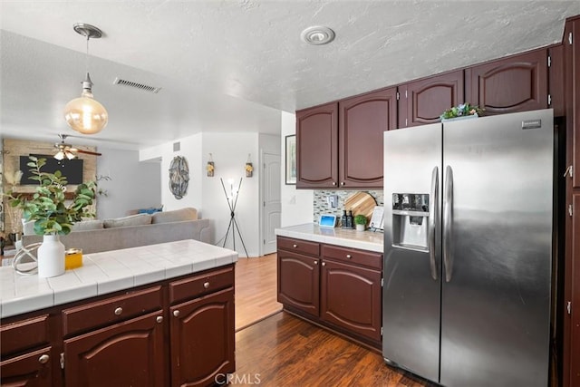 kitchen featuring visible vents, open floor plan, stainless steel refrigerator with ice dispenser, tile countertops, and dark wood-type flooring