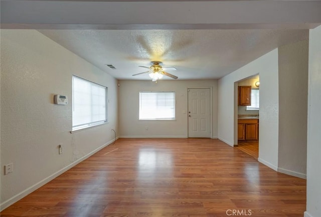 interior space with visible vents, light wood-style floors, baseboards, a textured ceiling, and a ceiling fan