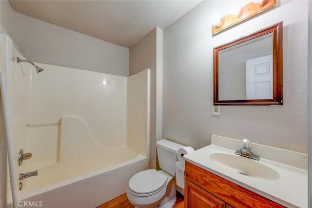 full bath with vanity, a textured wall, shower / bathtub combination, and toilet