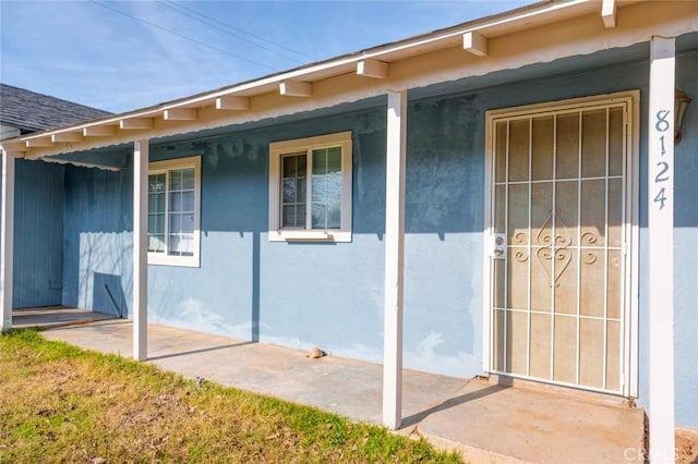 property entrance featuring covered porch and stucco siding