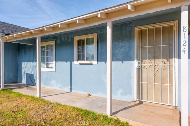 doorway to property featuring a porch, a shingled roof, and stucco siding