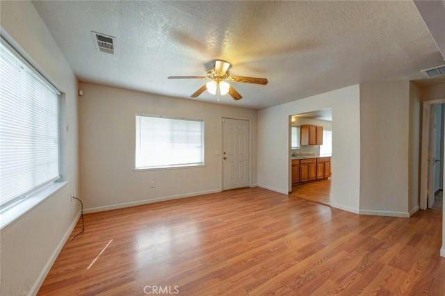 empty room with visible vents, baseboards, light wood-style floors, a textured ceiling, and a ceiling fan