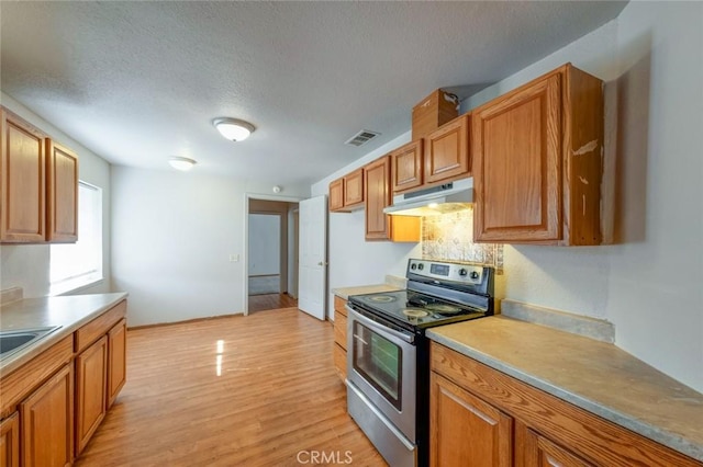 kitchen with a textured ceiling, visible vents, light wood finished floors, electric stove, and under cabinet range hood