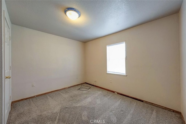 carpeted spare room featuring a textured ceiling and baseboards