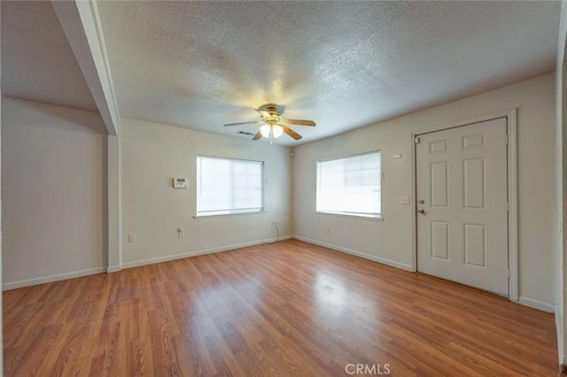 interior space with light wood-style floors, baseboards, a ceiling fan, and a textured ceiling