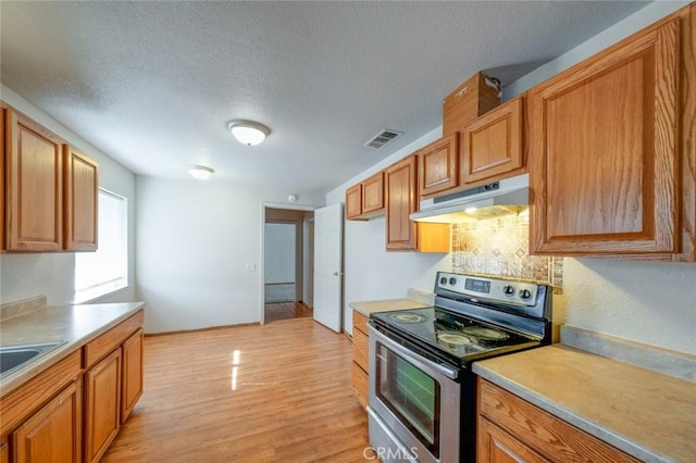 kitchen featuring visible vents, stainless steel range with electric stovetop, light countertops, under cabinet range hood, and light wood-style flooring