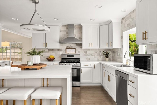 kitchen featuring light countertops, a sink, white cabinets, wall chimney range hood, and appliances with stainless steel finishes