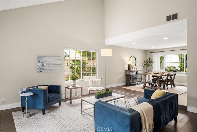 living room with a high ceiling, baseboards, visible vents, and wood finished floors