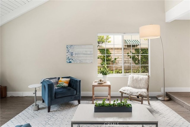 living area featuring wood finished floors, baseboards, and vaulted ceiling with beams