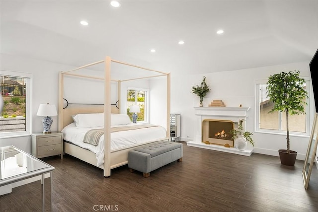 bedroom featuring multiple windows, a lit fireplace, recessed lighting, and dark wood-style floors