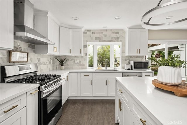 kitchen featuring dark wood finished floors, a sink, white cabinetry, wall chimney range hood, and stainless steel appliances