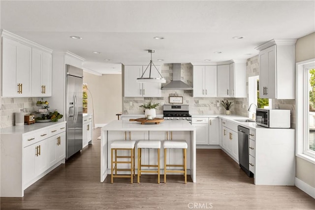 kitchen with a center island, a sink, wall chimney exhaust hood, stainless steel appliances, and decorative backsplash