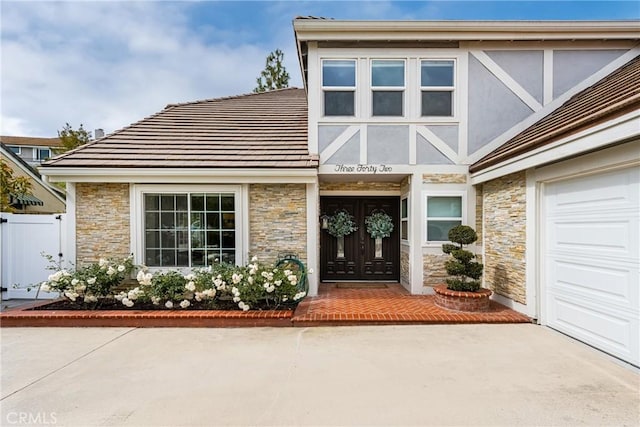 view of front of property with fence, stone siding, a tile roof, concrete driveway, and a garage