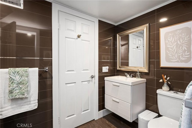 half bath with tile walls, toilet, vanity, ornamental molding, and visible vents