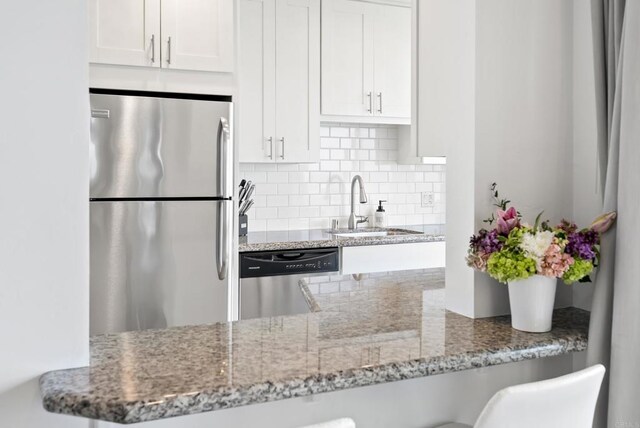 kitchen with appliances with stainless steel finishes, tasteful backsplash, a sink, light stone counters, and white cabinets