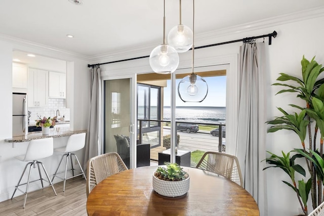 dining space featuring light wood-type flooring, ornamental molding, a water view, and recessed lighting