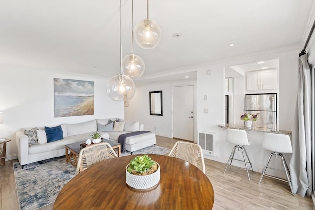 dining area with crown molding, baseboards, light wood-style flooring, and visible vents