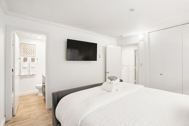 bedroom featuring light wood finished floors, baseboards, ensuite bathroom, ornamental molding, and a closet