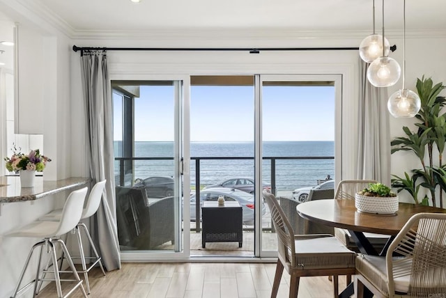dining area with a water view, ornamental molding, and light wood-style floors